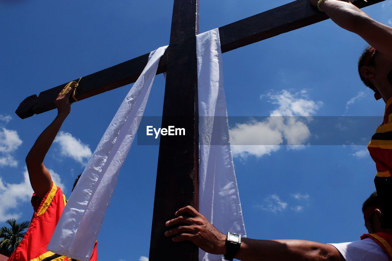 Cross with scarf amidst people against blue sky