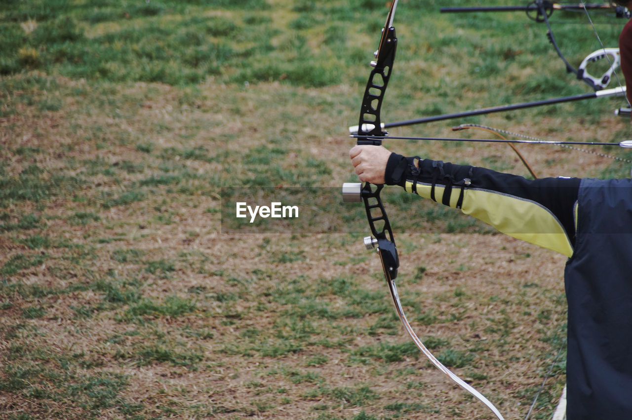 Midsection of person aiming with archery bow while standing on field