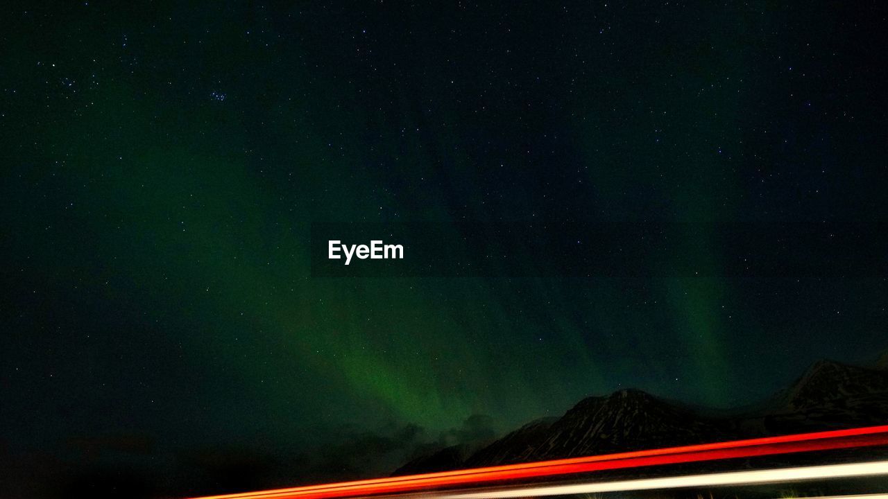 LIGHT TRAILS AGAINST MOUNTAIN AT NIGHT