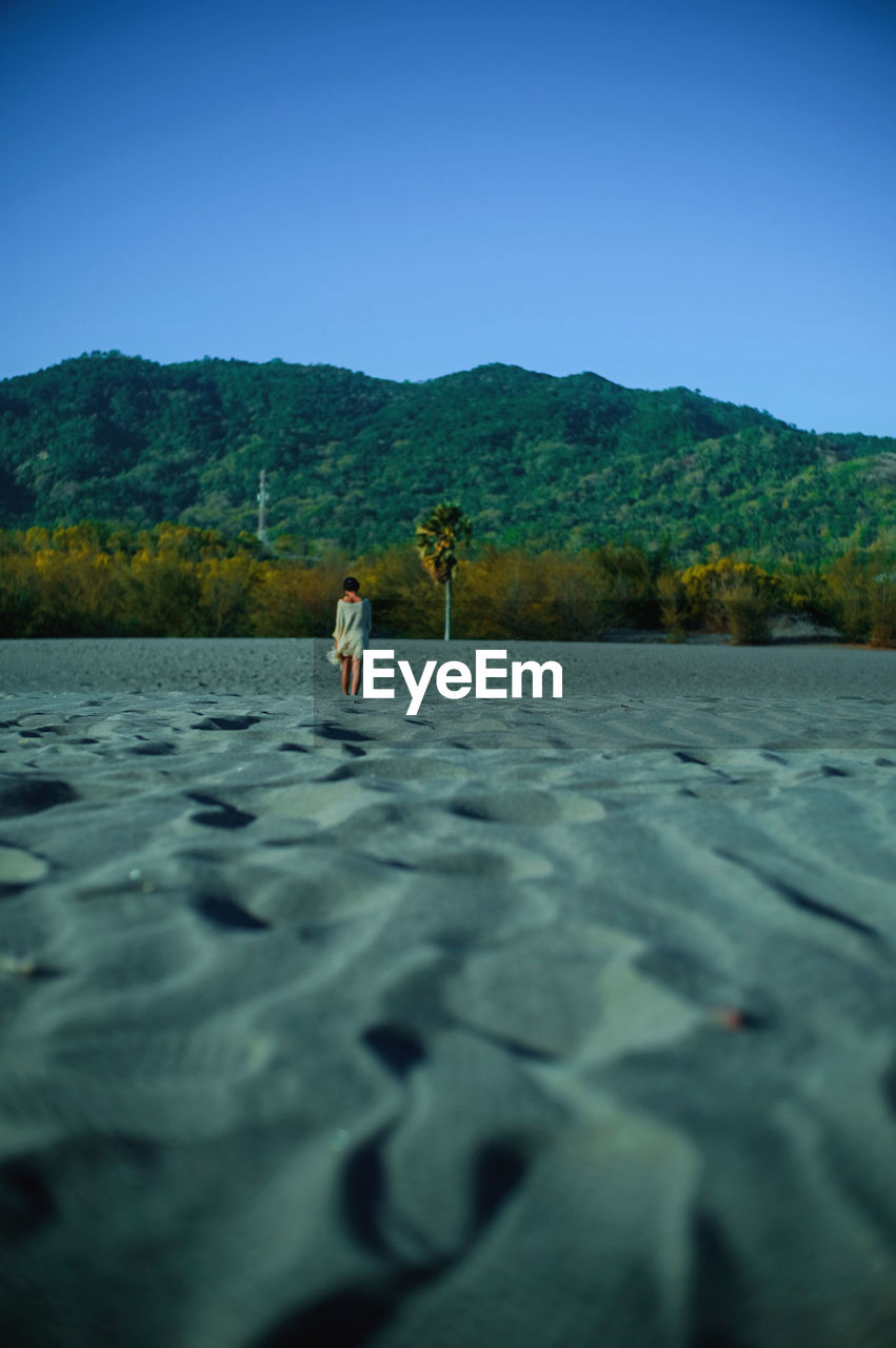 Rear view of woman standing on sandy beach against clear sky