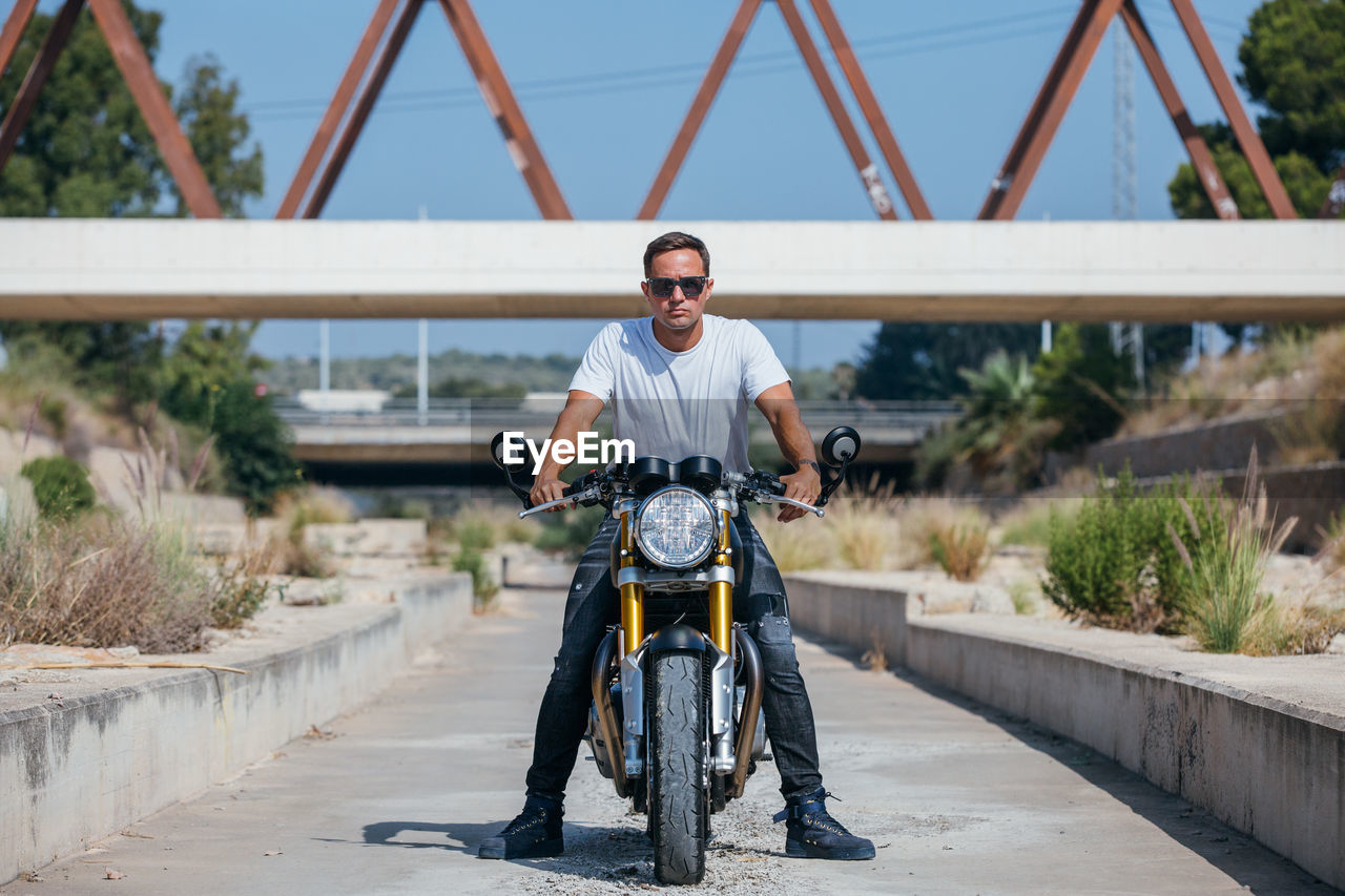 Stylish male biker sitting on modern motorcycle in urban area and looking at camera