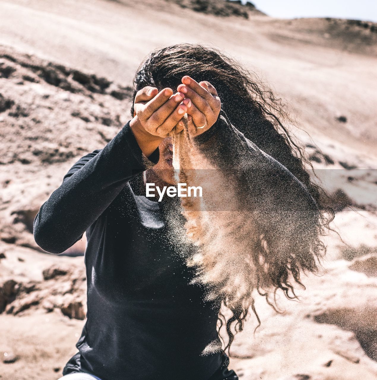 Woman with falling sand from hands at desert