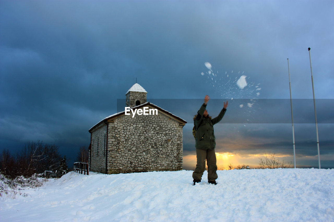 REAR VIEW OF PERSON STANDING ON SNOW COVERED FIELD