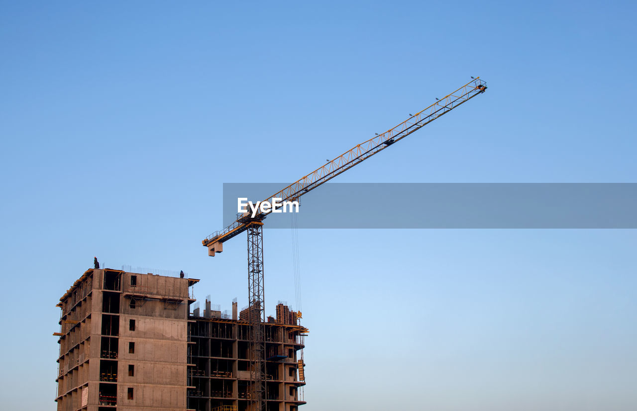 LOW ANGLE VIEW OF CRANE BY BUILDING AGAINST CLEAR SKY