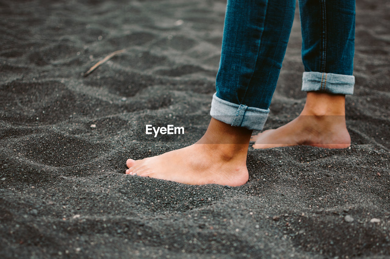 Anonymous barefoot female in jeans standing on black volcanic soil on beach of la palma island in spain