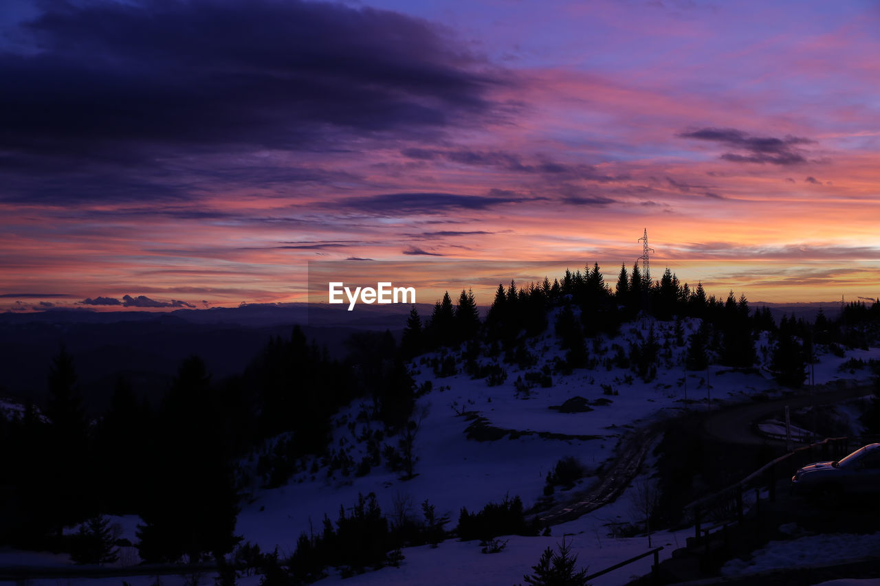 Scenic view of snow covered mountains against orange purple sunset sky