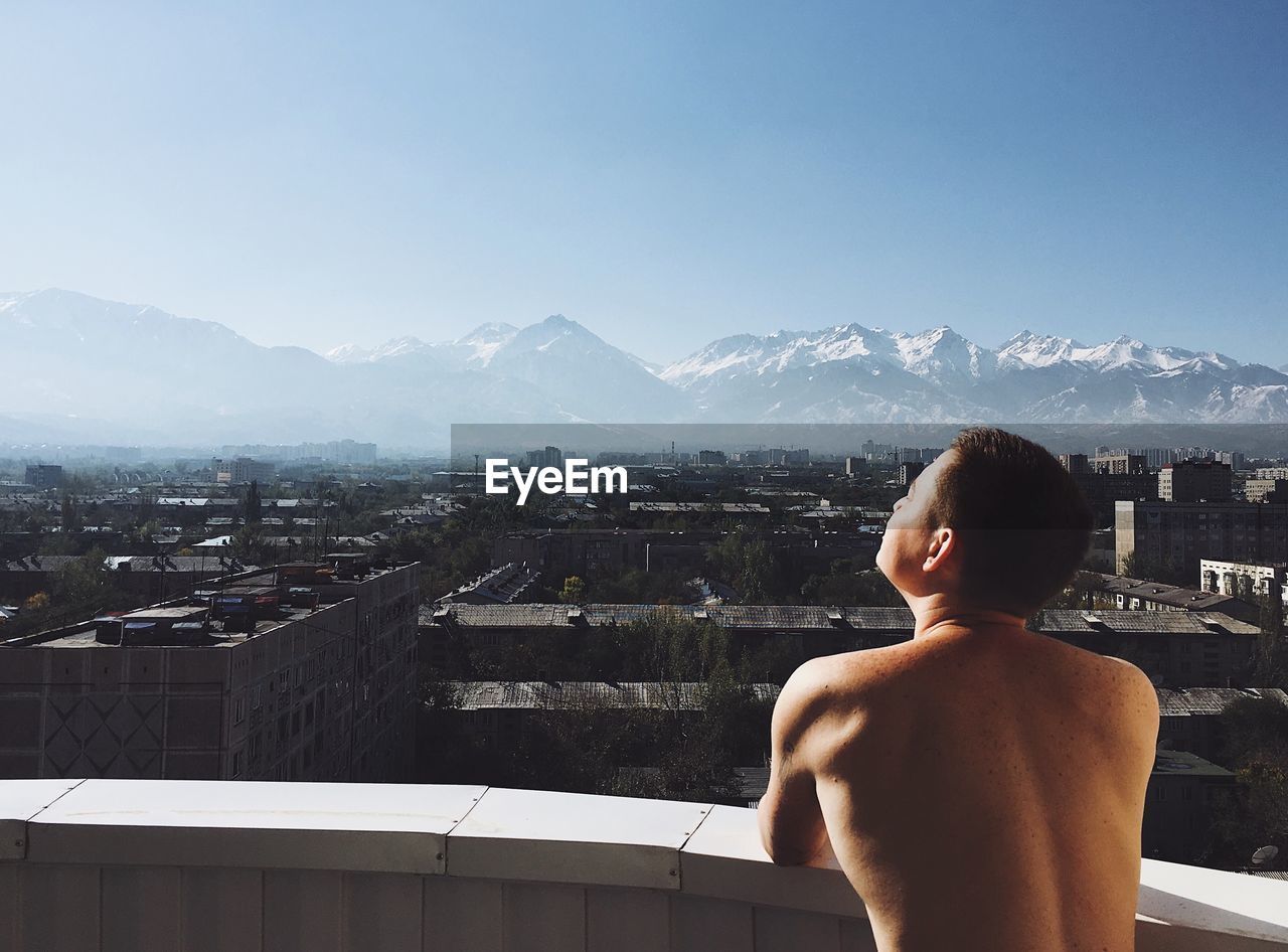 Rear view of shirtless man looking at cityscape against sky