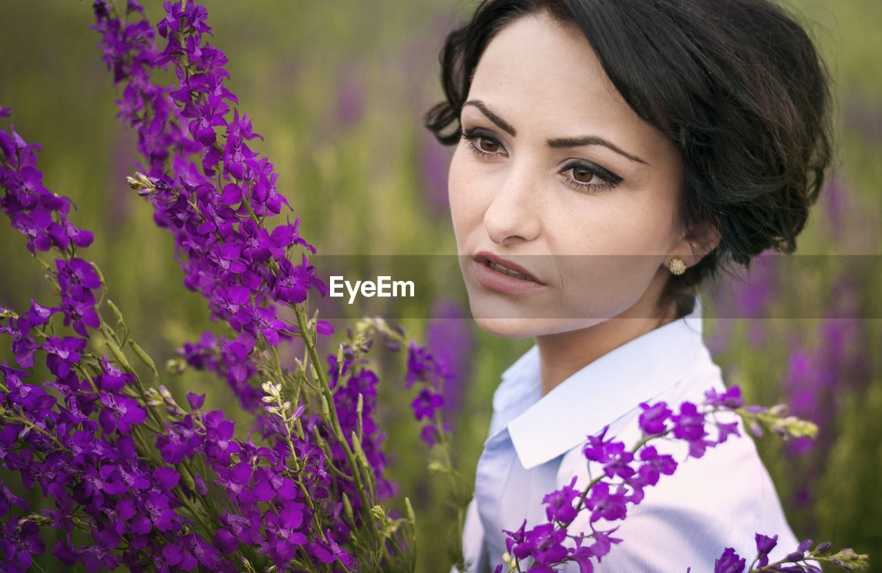 Close-up of young woman by purple flowers on field