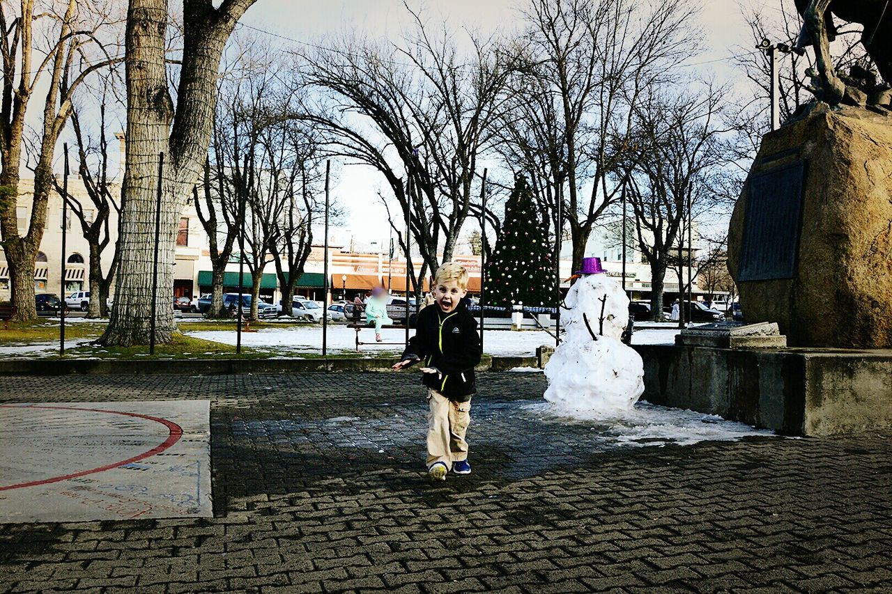 Portrait of boy playing by snowman on sidewalk