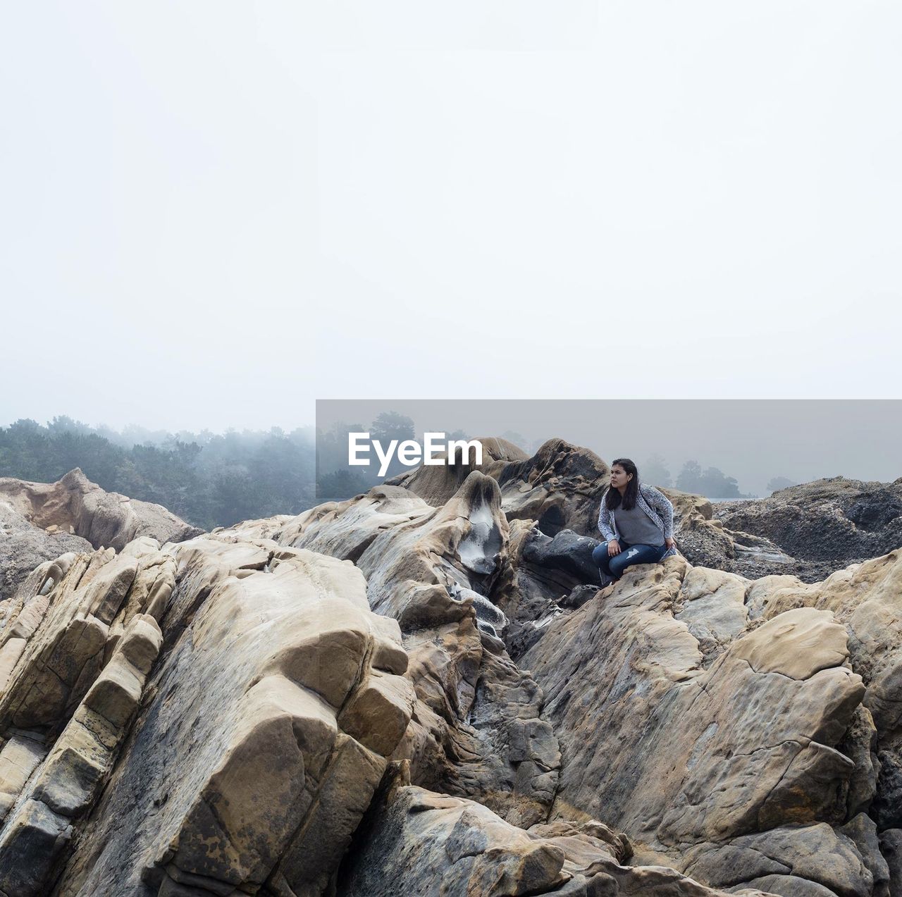 Woman sitting on rock against clear sky