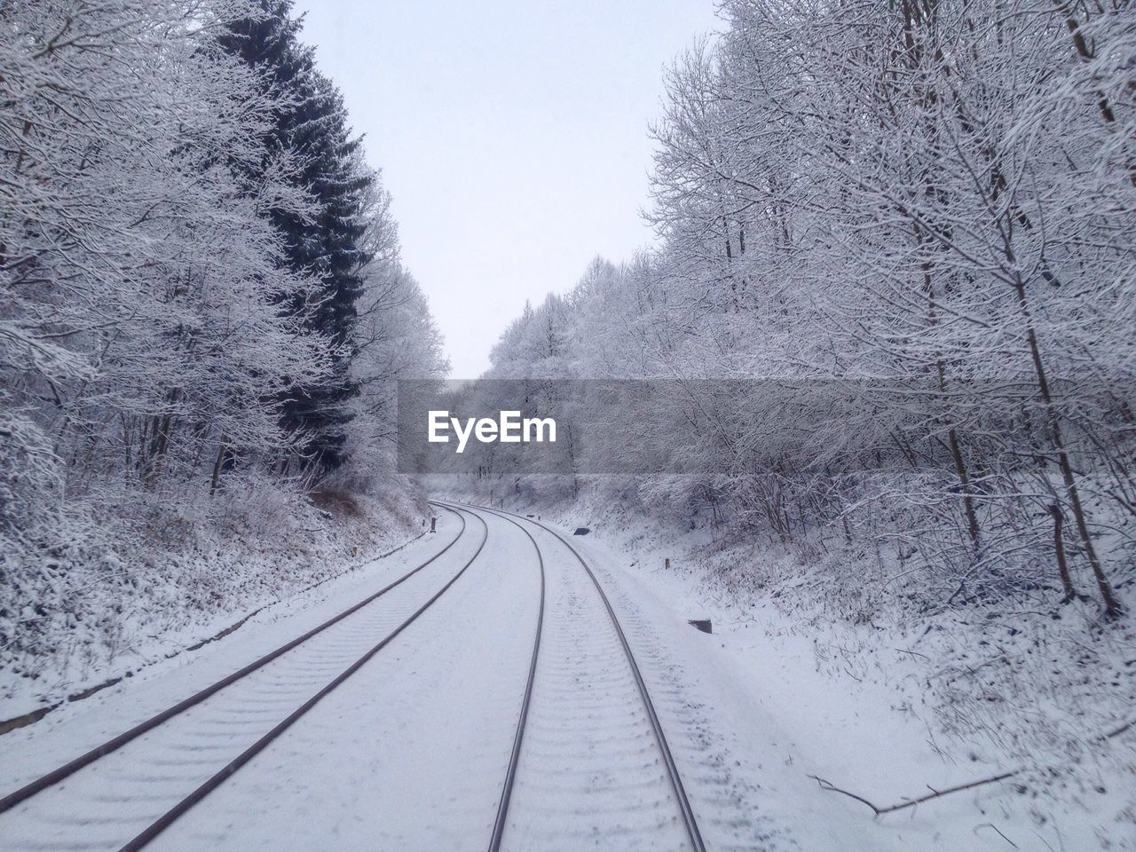 Snow covered railway tracks and bare trees against clear sky