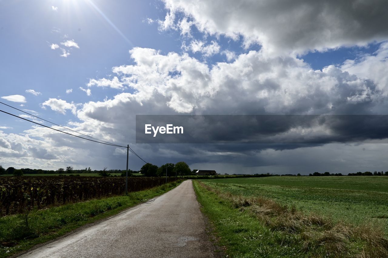 sky, cloud, landscape, environment, road, horizon, nature, plant, field, rural area, land, rural scene, transportation, grass, beauty in nature, the way forward, agriculture, sunlight, scenics - nature, no people, cloudscape, dirt road, outdoors, diminishing perspective, vanishing point, dirt, tranquility, dramatic sky, crop, day, morning, plain, blue, farm, tree, hill, non-urban scene, country road, storm, prairie, growth, travel