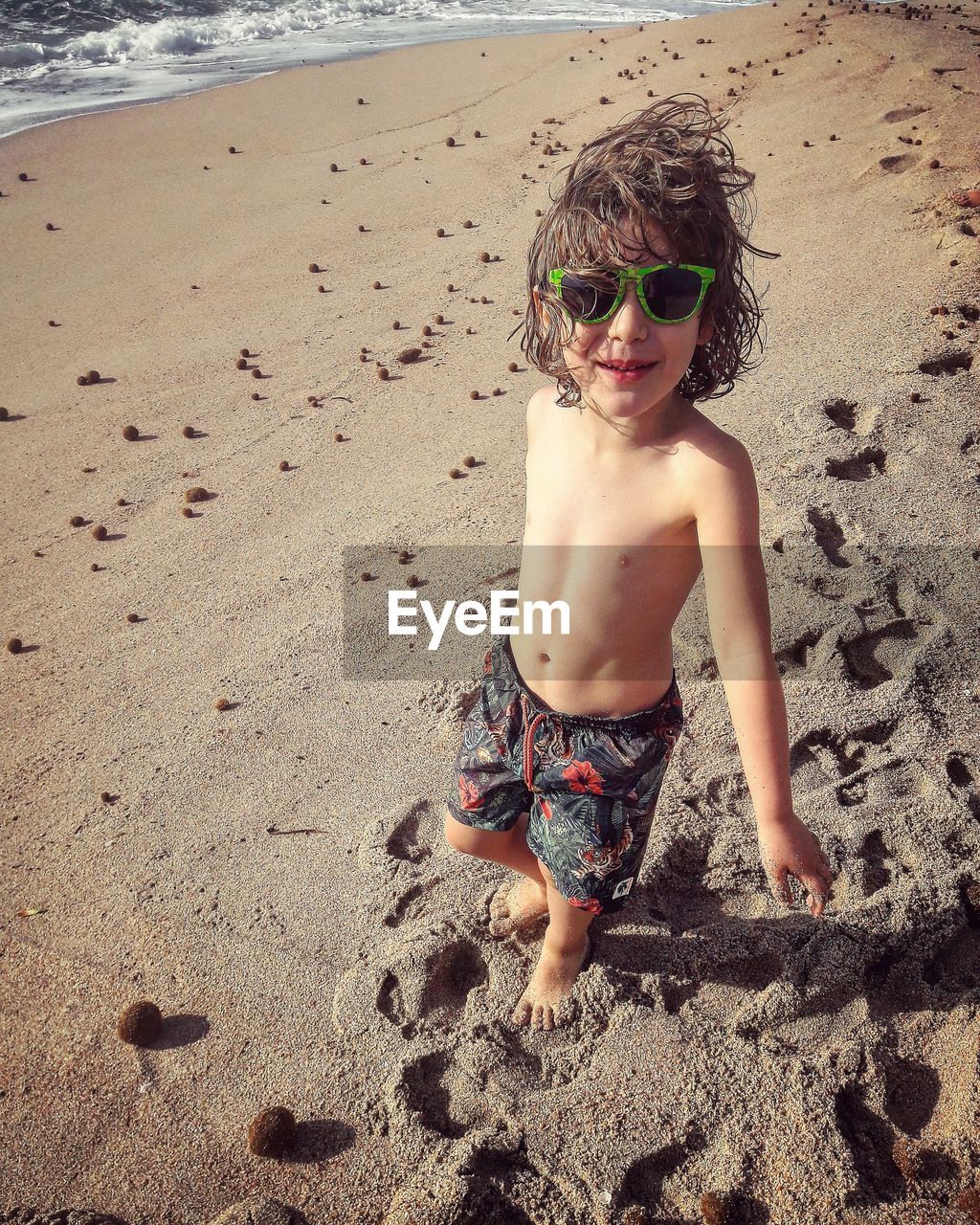 High angle portrait of shirtless boy wearing sunglasses standing at beach