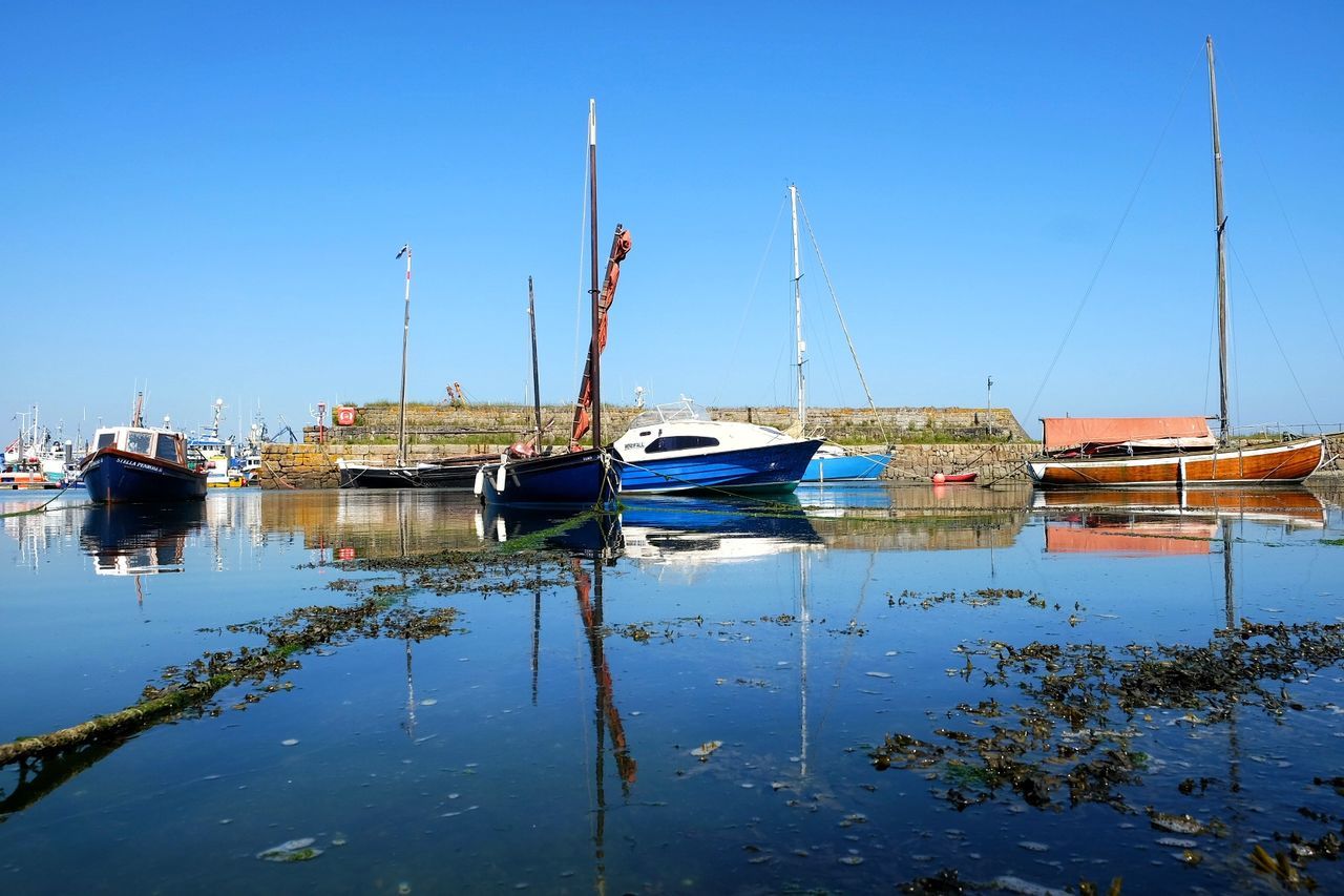 Boats moored at harbor against clear blue sky