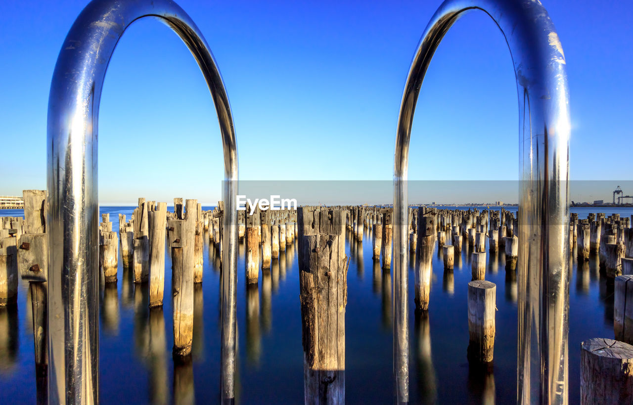 Railing against wooden posts in sea against clear sky