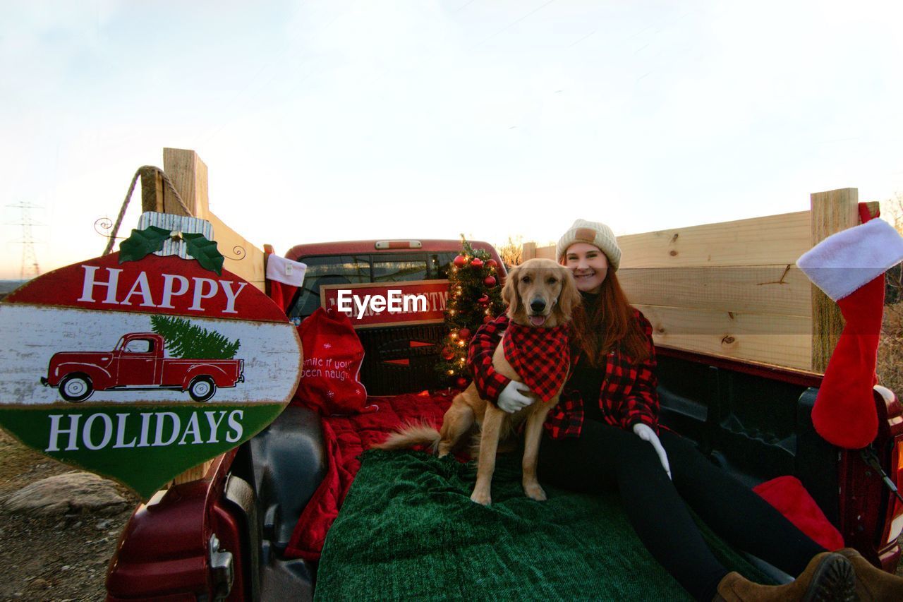 Woman with dog and christmas tree sitting on truck outdoors