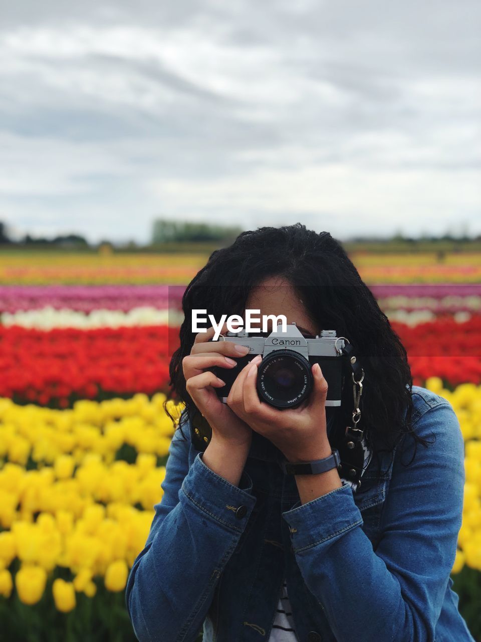 Portrait of woman photographing with camera on field against cloudy sky