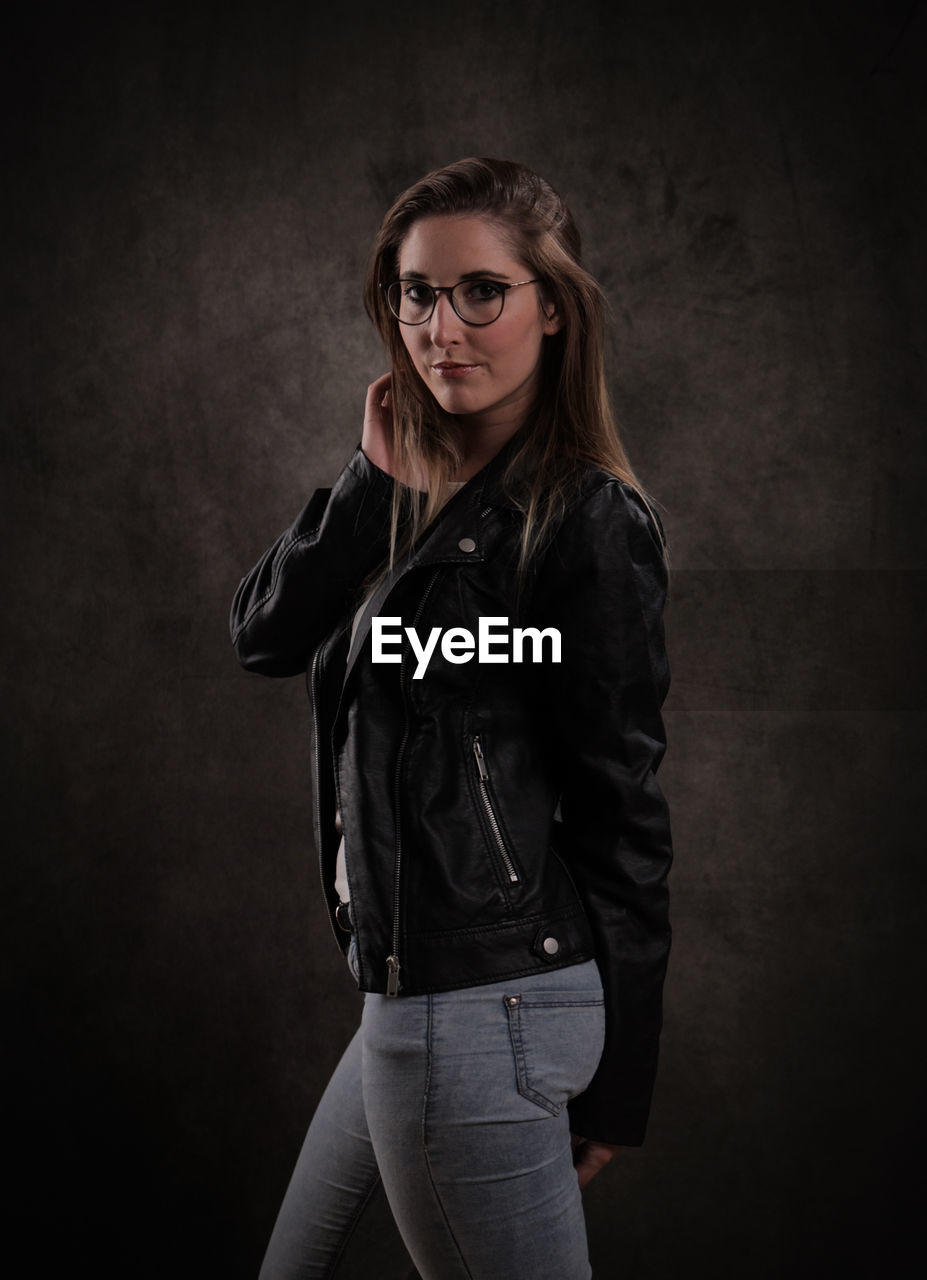 portrait of young woman standing against black wall