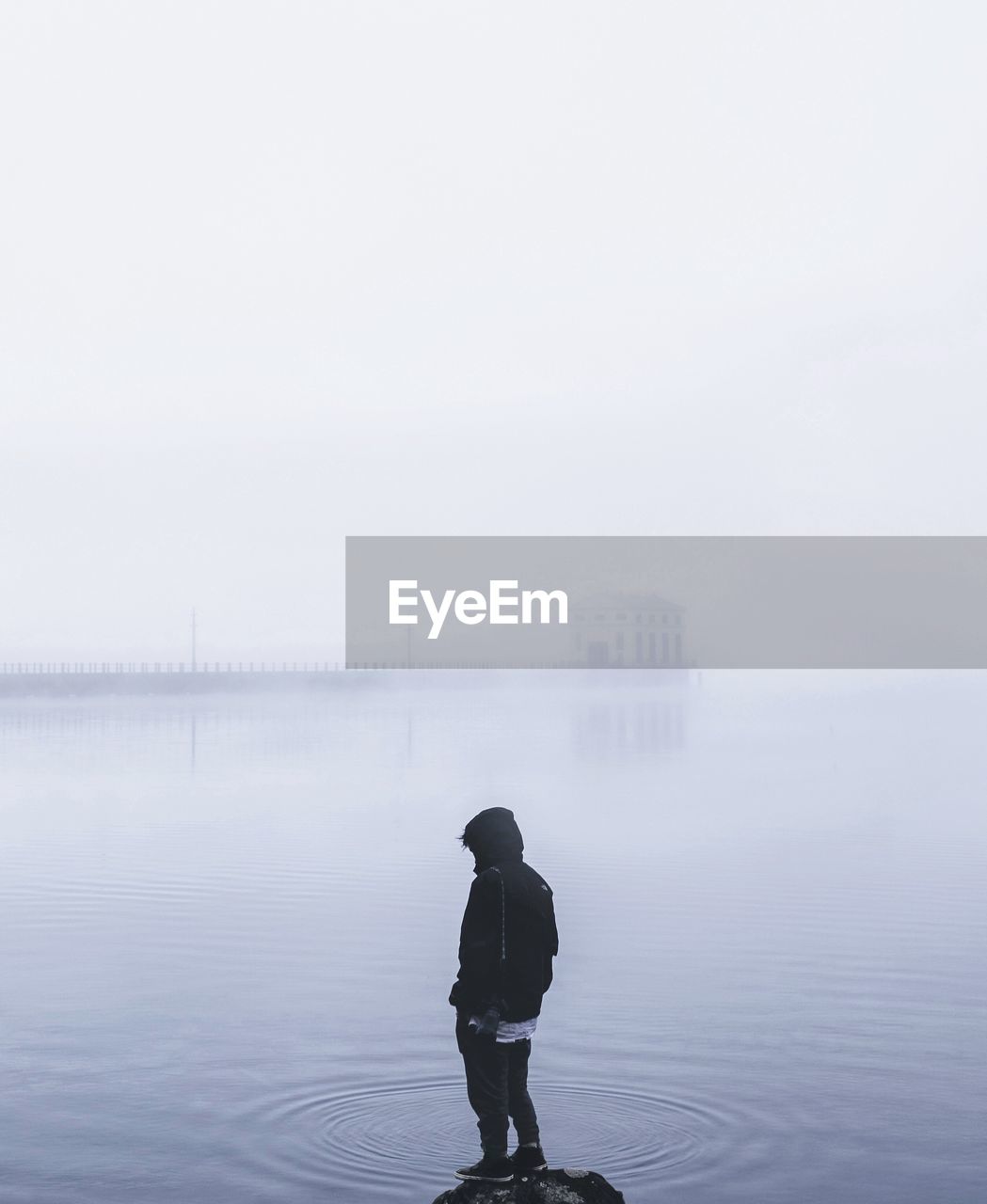 Rear view of person standing in lake during foggy weather