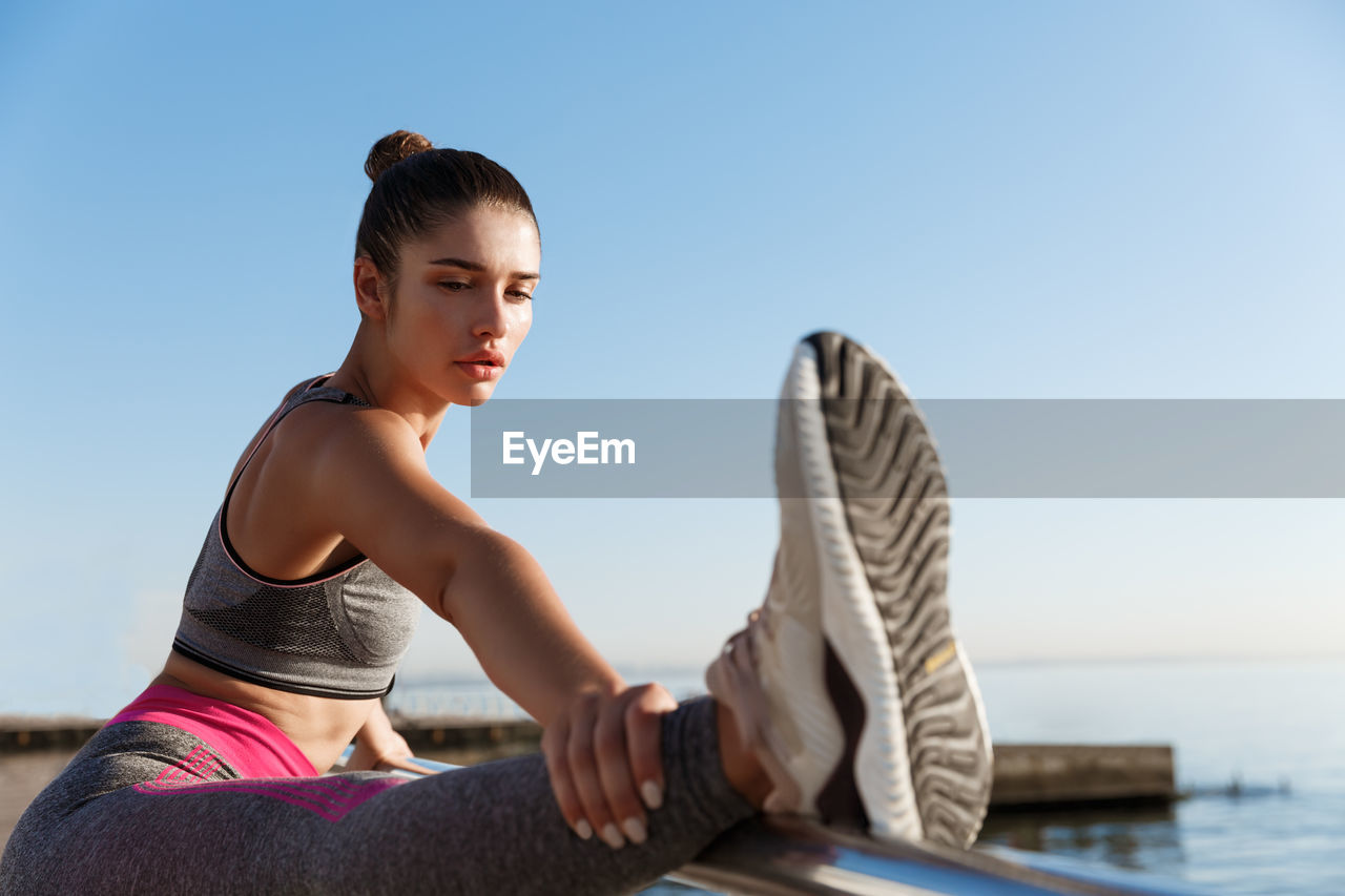 Woman stretching on railing against sky