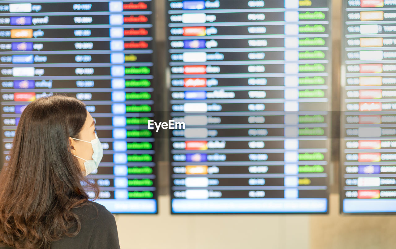 Rear view of woman wearing mask looking at departure board