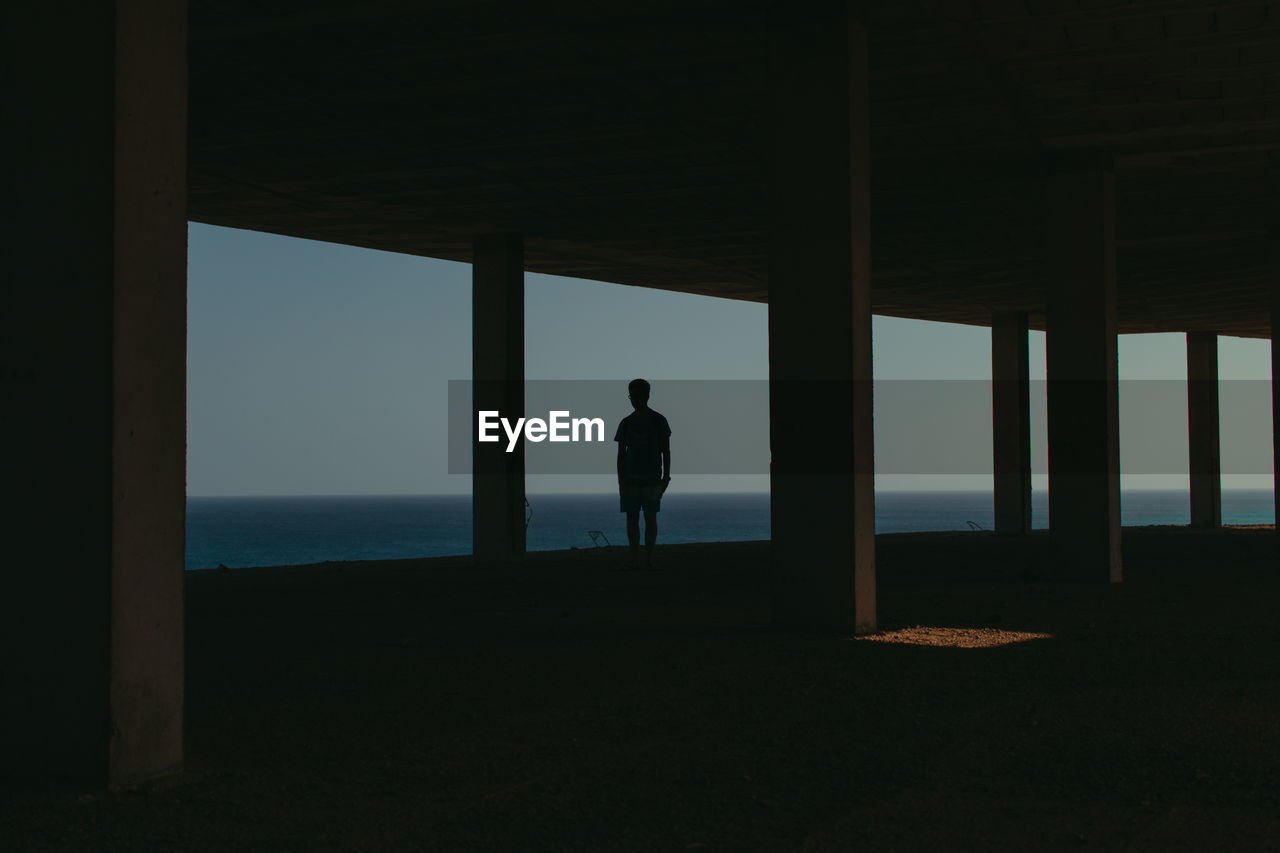 Silhouette man standing by window while looking at sea