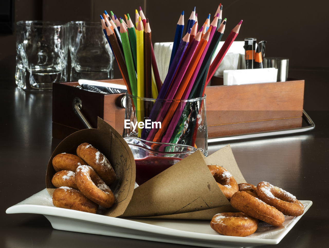 Sprinkling sugar powder donuts and colored pencils in container on table