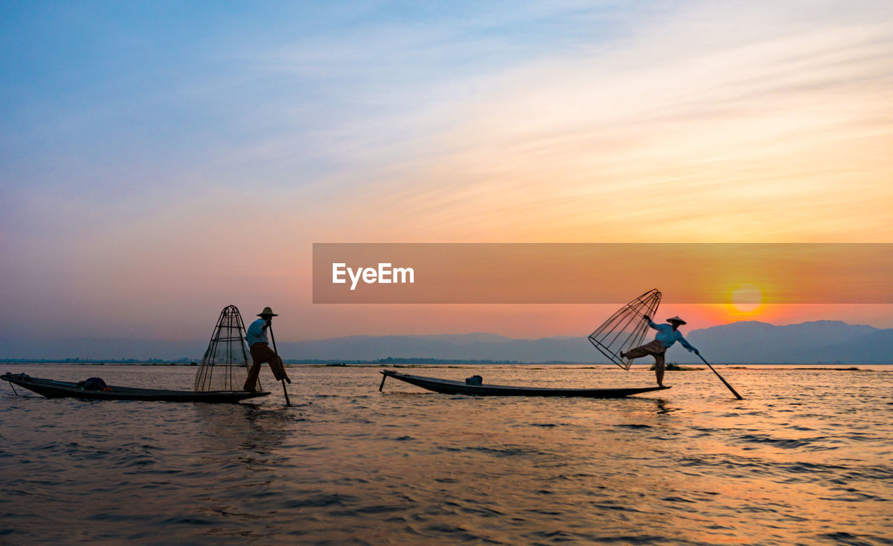 Fishermen fishing in sea during sunset against sky