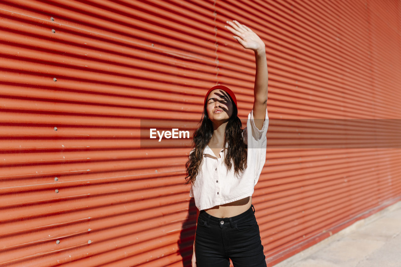 Woman with hand raised shielding face on sunny day