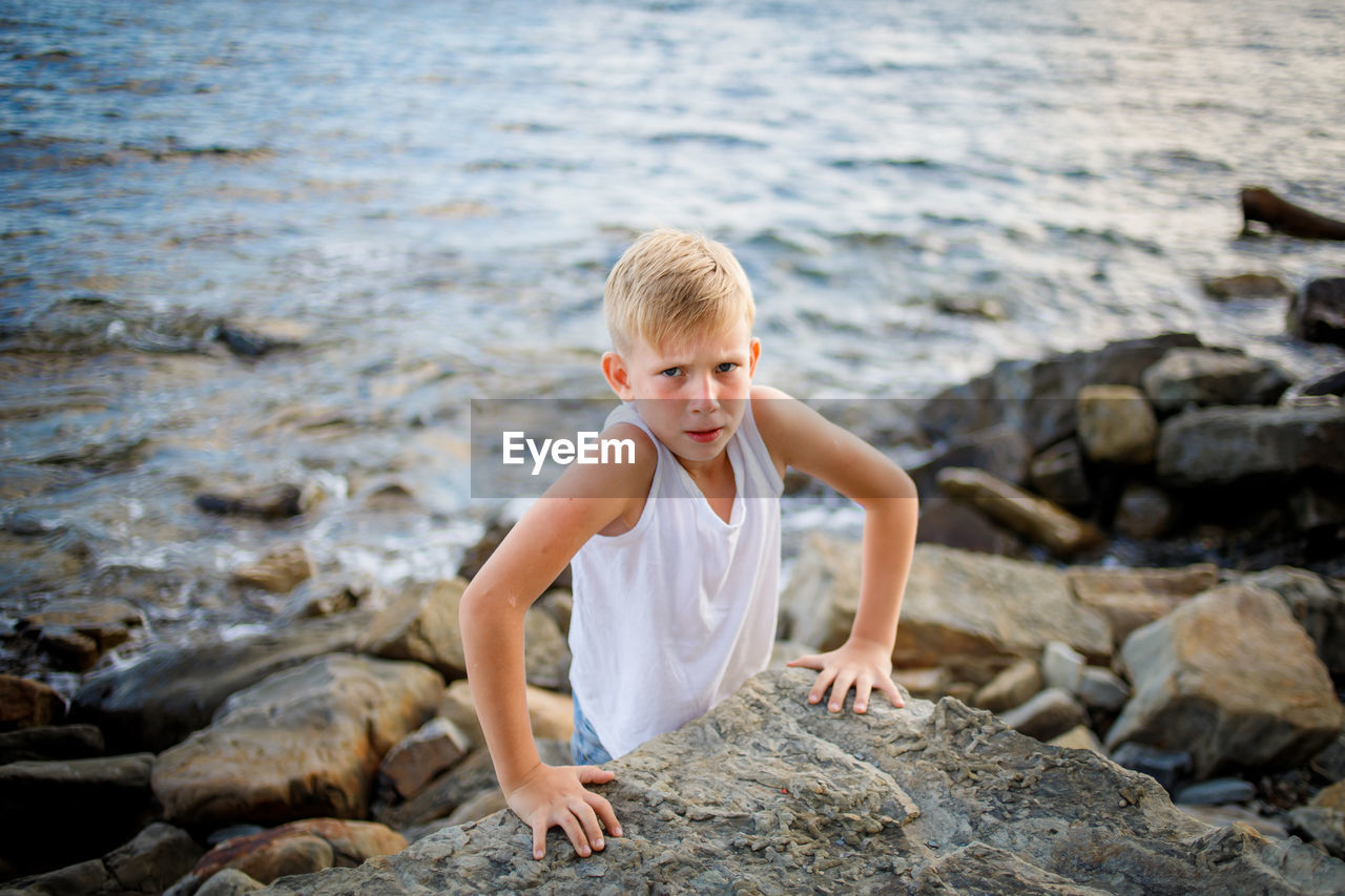 BOY ON ROCK AT SHORE