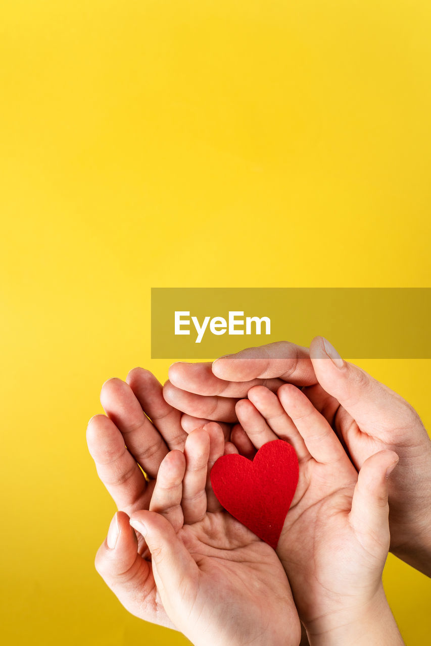 CLOSE-UP OF MAN HOLDING HANDS OVER YELLOW BACKGROUND AGAINST ORANGE GRAY