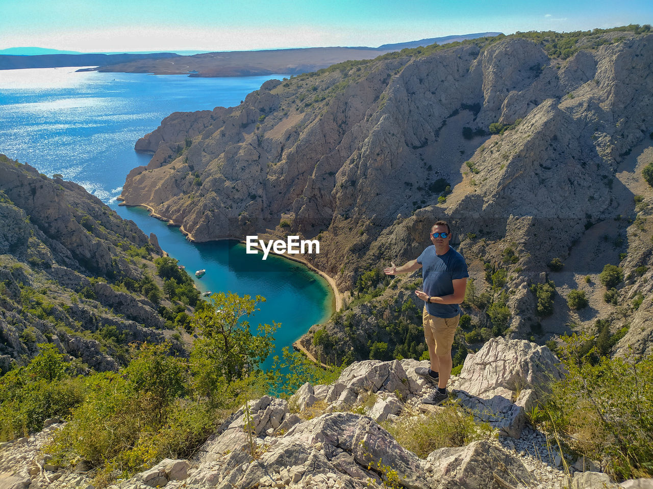 MAN STANDING ON ROCKS AGAINST MOUNTAIN