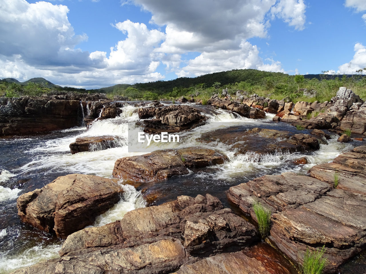 Scenic view of river flowing through rocks against sky