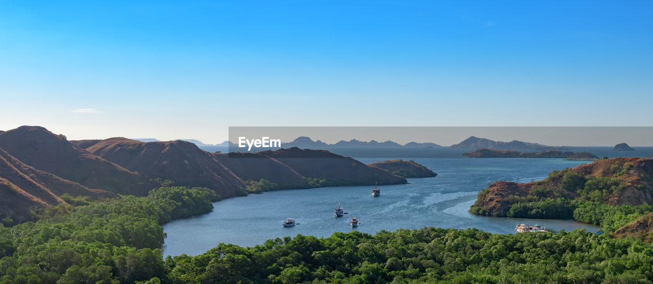 Scenic view of sea and mountains against clear blue sky