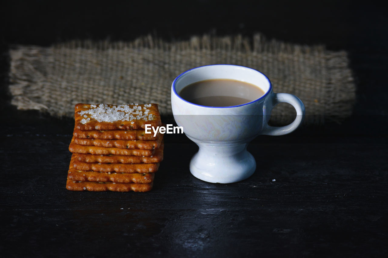 A cup of tea with biscuits on old wooden dark background