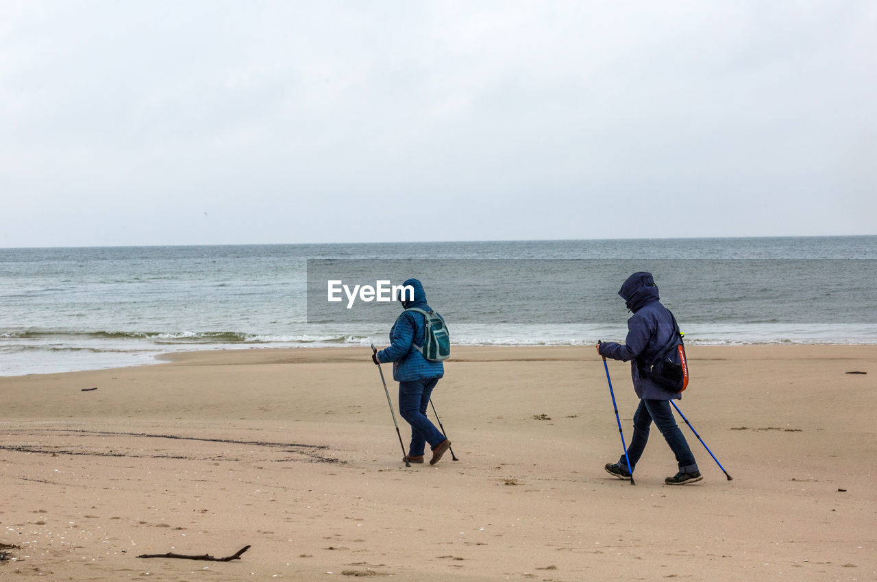 People with walking poles at beach against sky