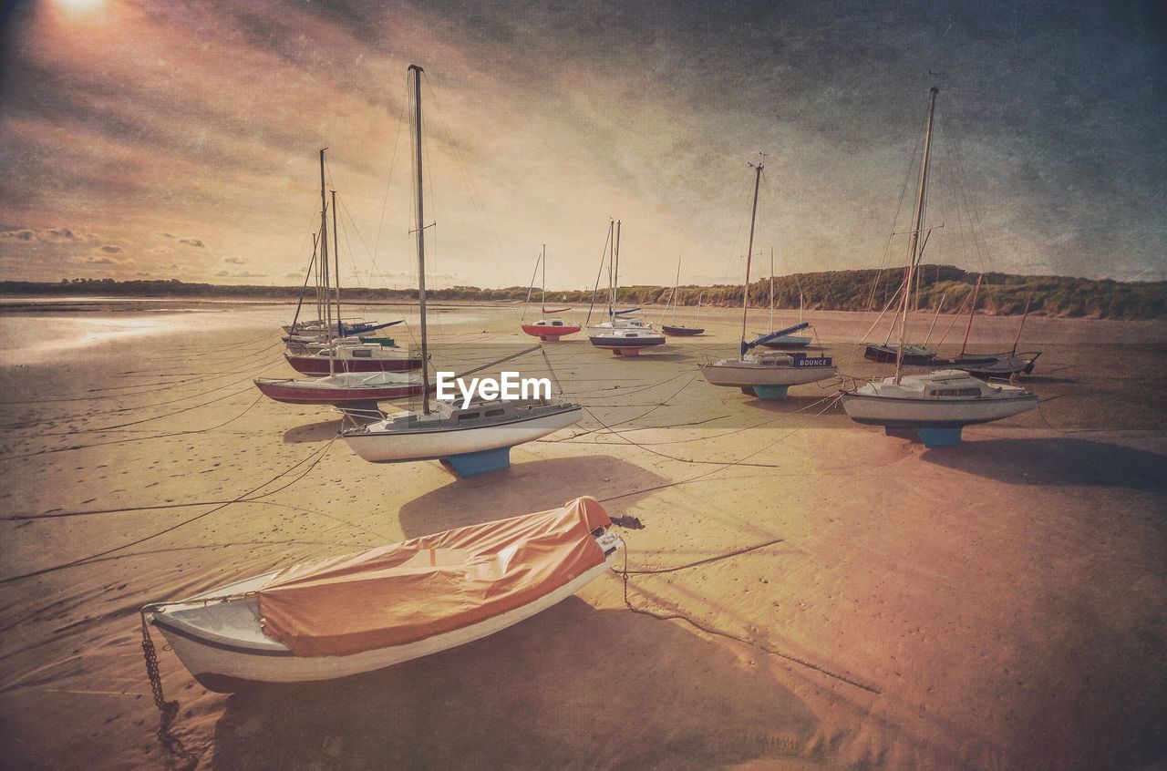 Boats moored on sand at beach against sky