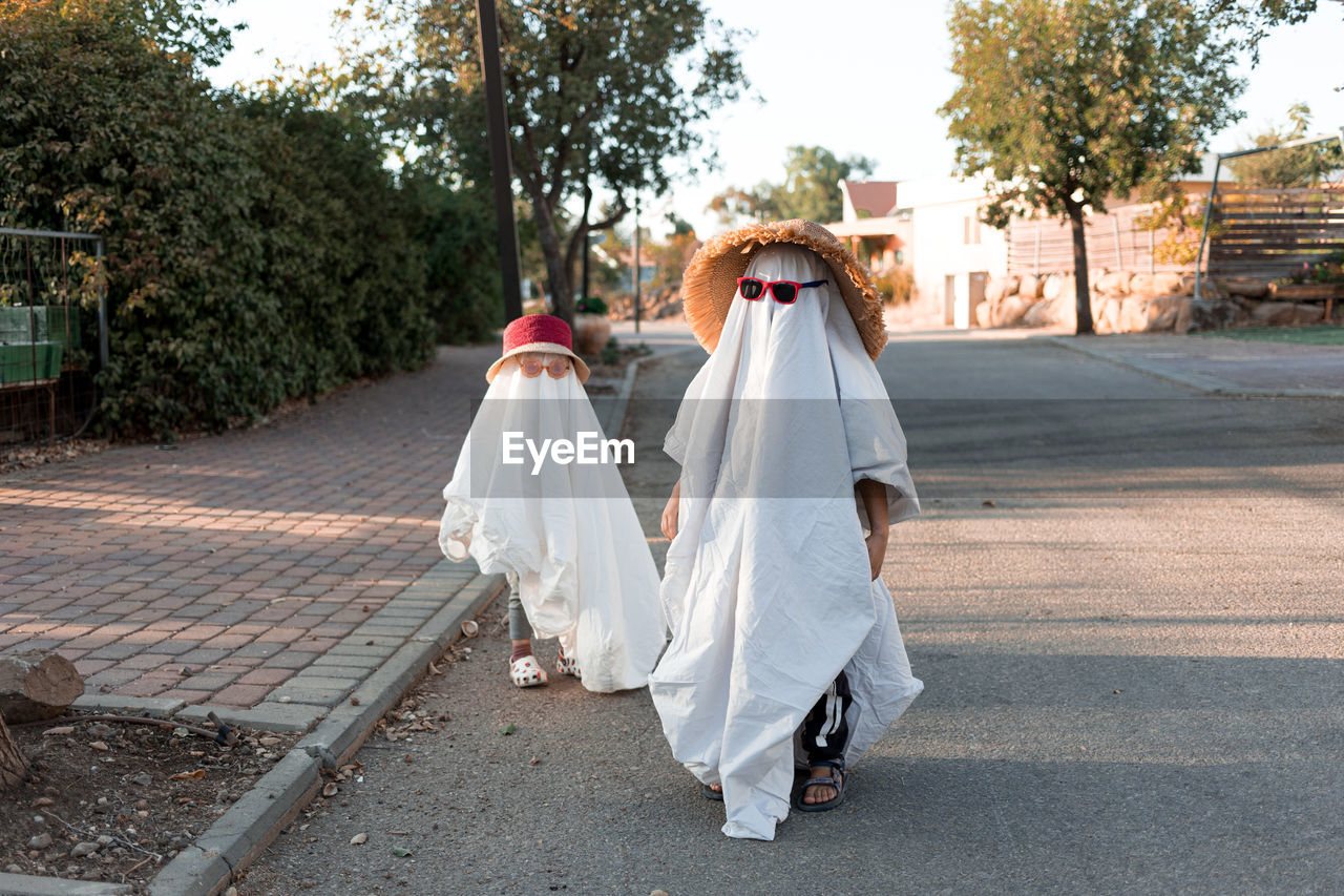 Trendy sheet ghosts costumes on little kids standing on a suburbs street. happy halloween holiday