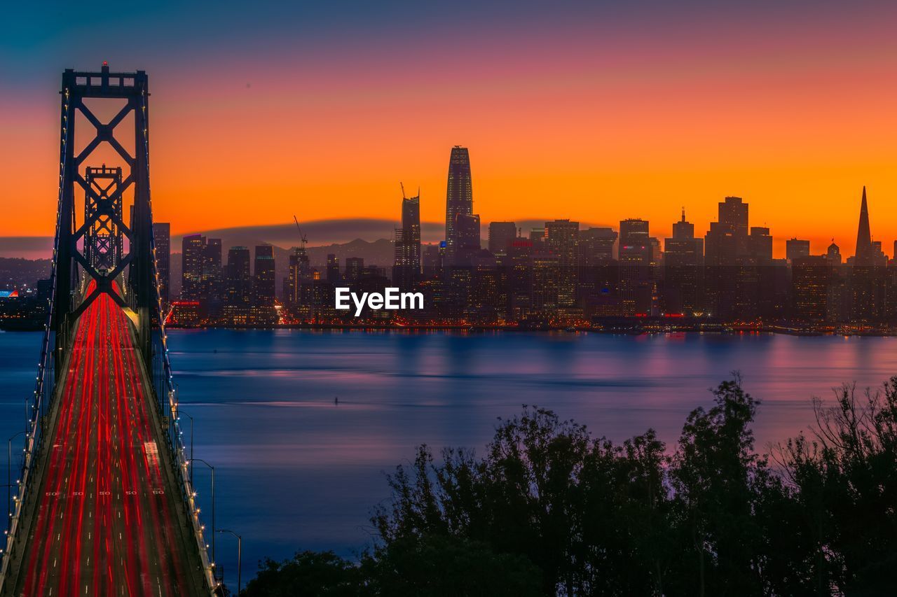 Illuminated city at waterfront during sunset