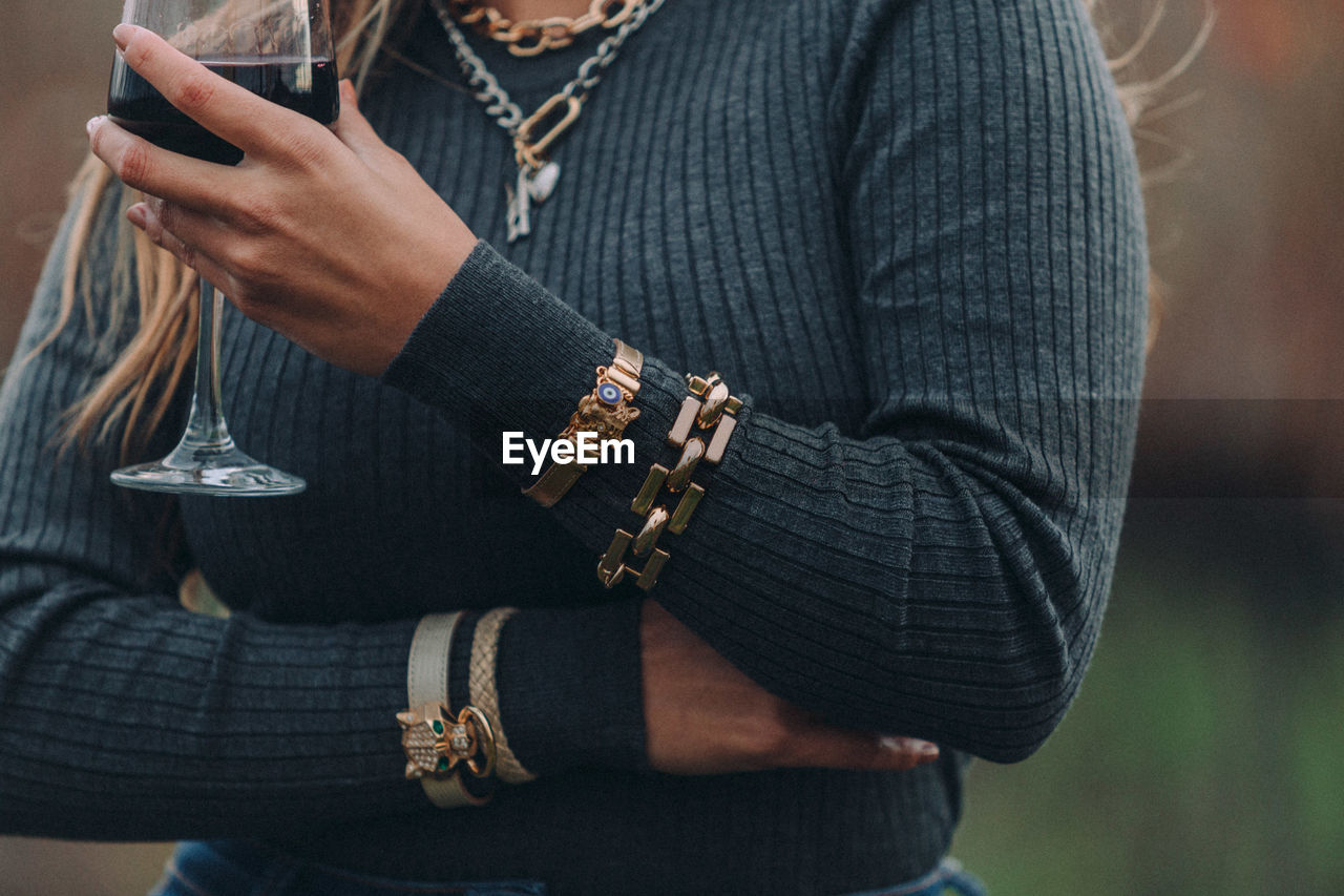 Midsection of woman in warm clothing wearing bracelet holding wineglass outdoors