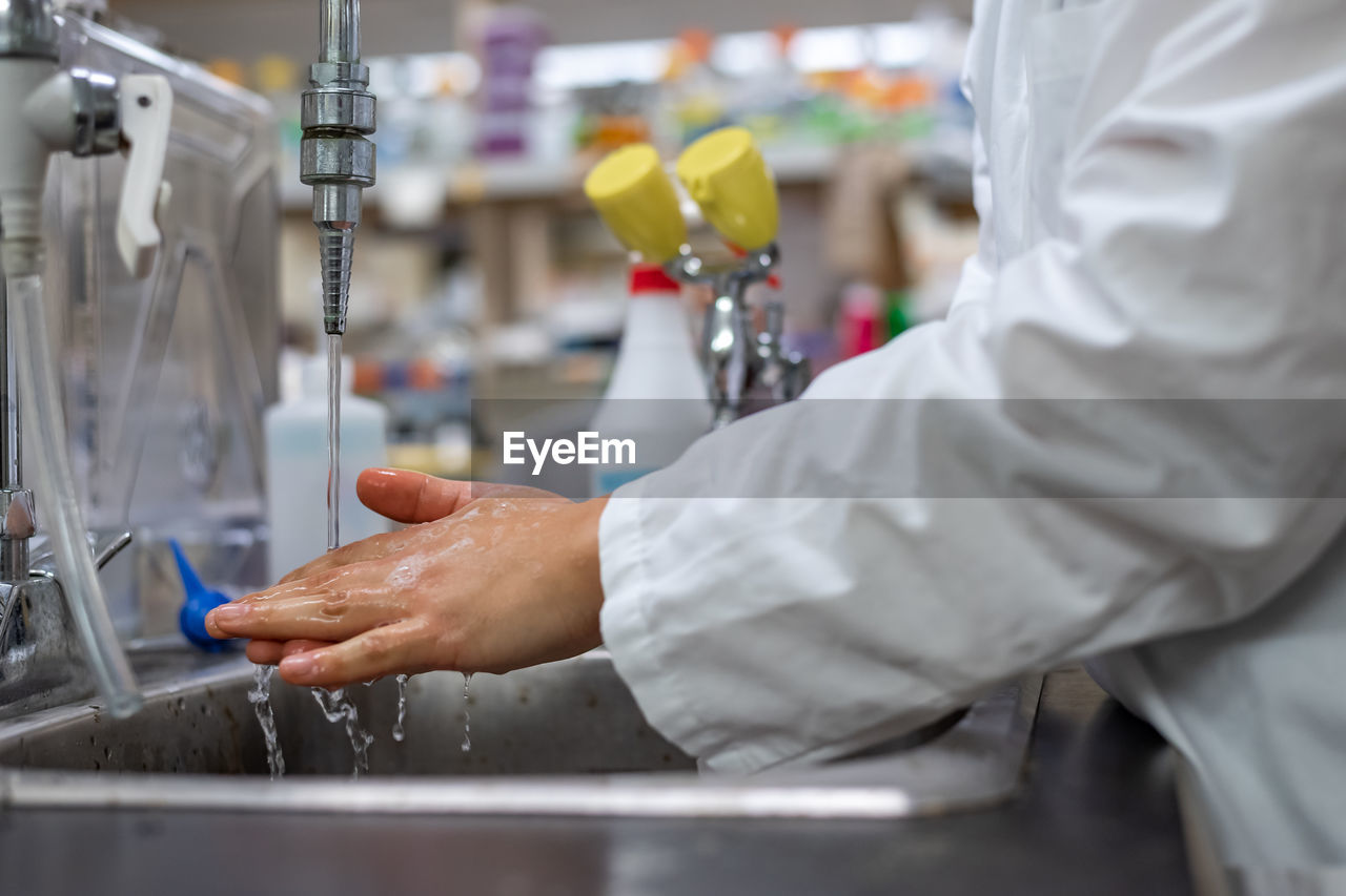 Side view midsection of doctor washing hands in sink at hospital