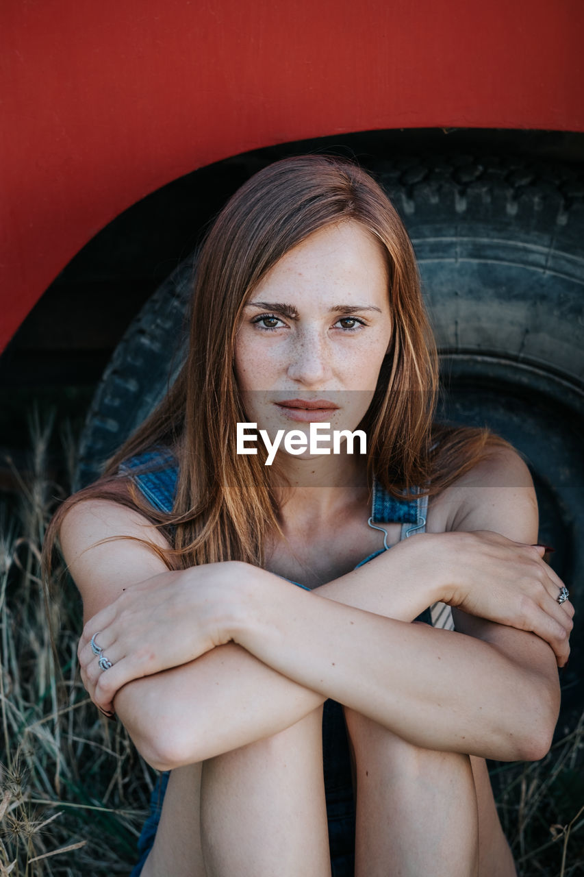 Portrait of young woman sitting against tire
