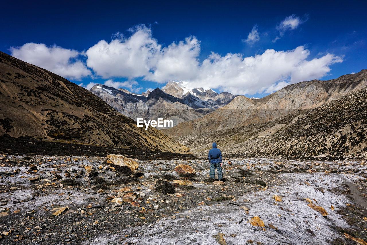 REAR VIEW OF PERSON WALKING ON ROCK AGAINST SKY