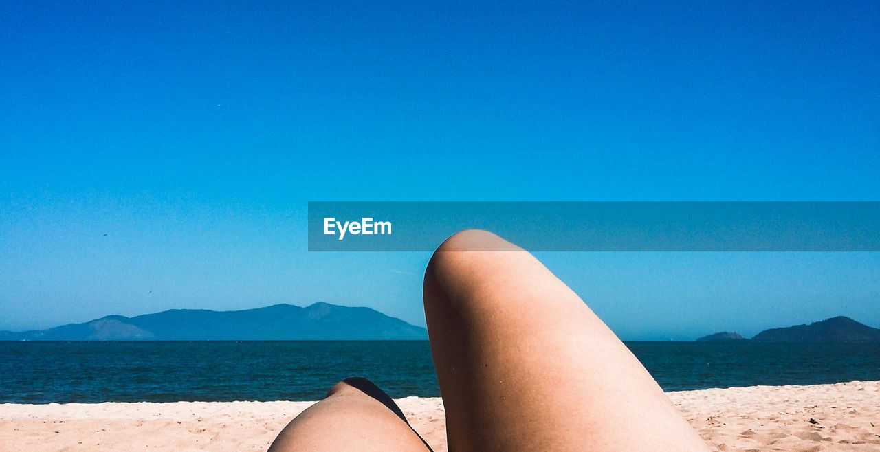 Low section of woman relaxing on beach against sky