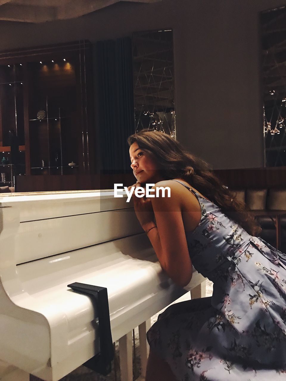 Young woman looking away leaning against grand piano at restaurant