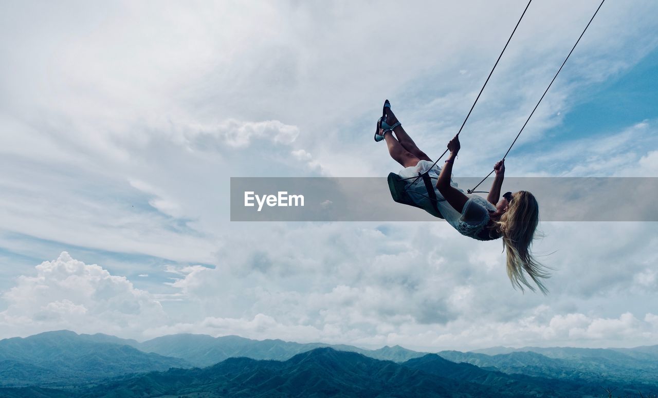 Low angle view of woman on swing against sky