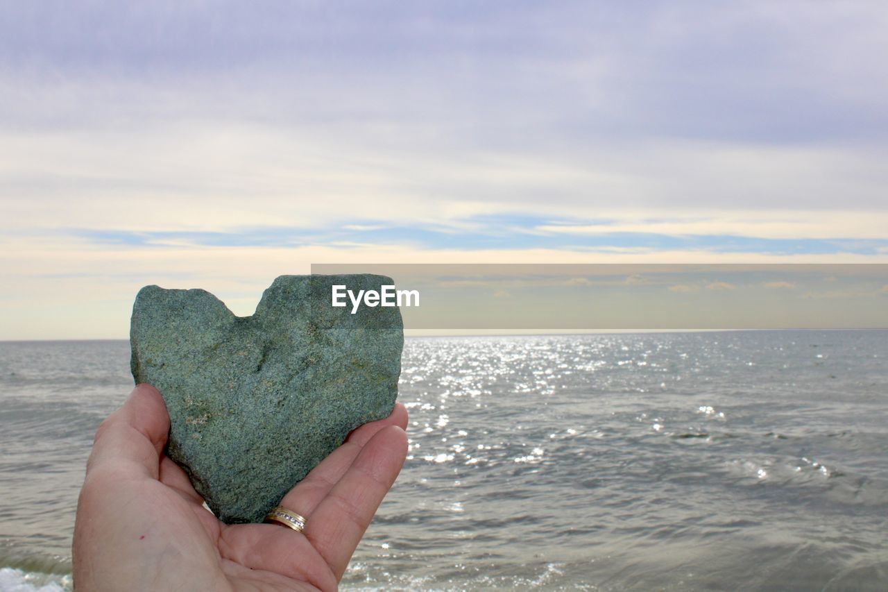 Hand of woman holding heart sea rock against sky