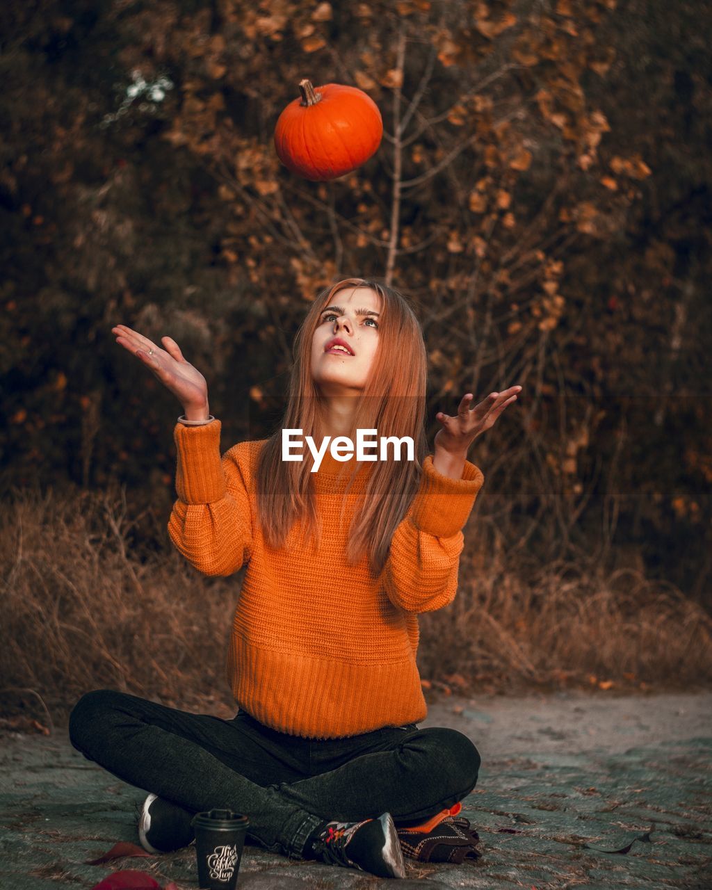 Full length of young woman holding pumpkin sitting against trees