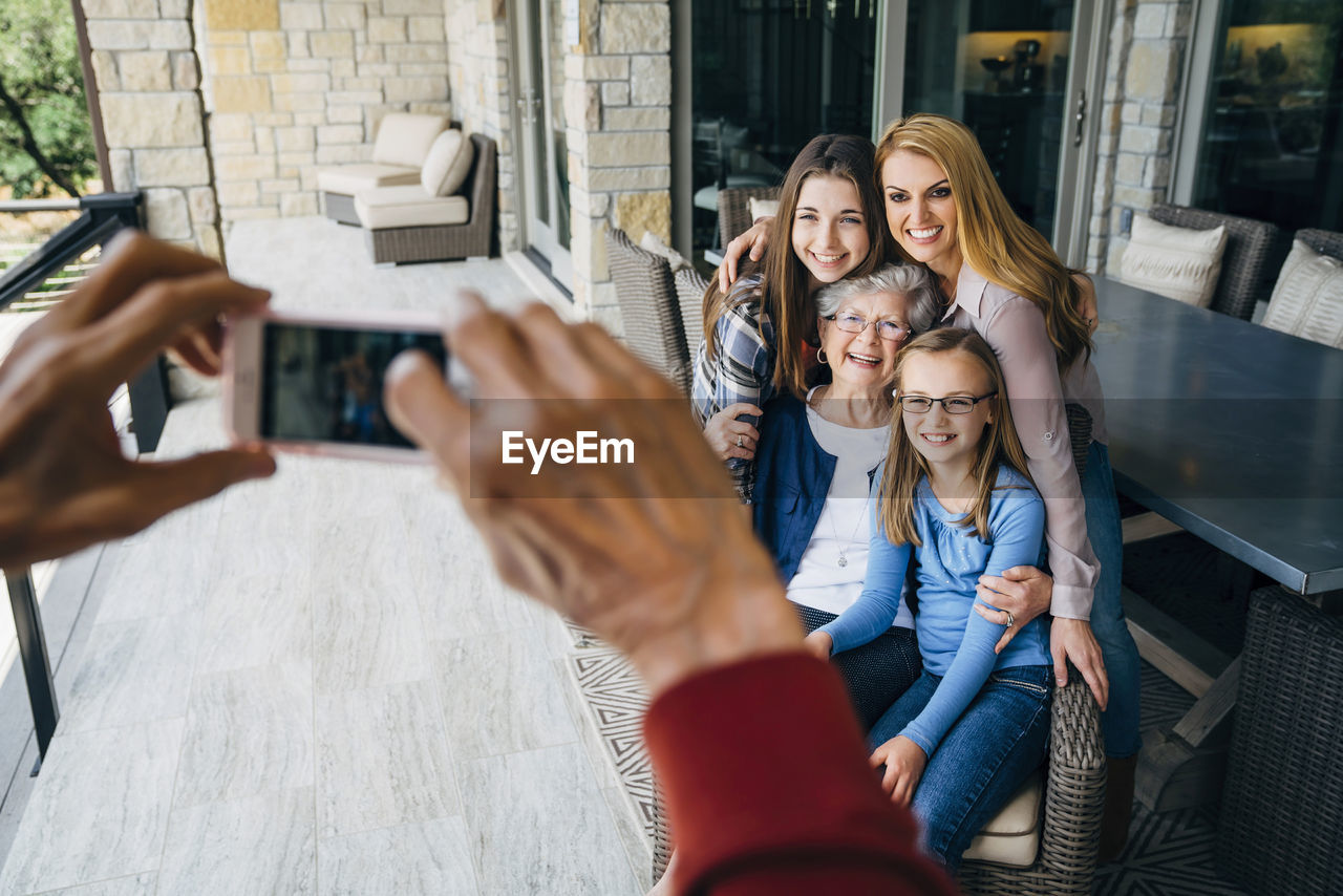 Cropped hands of senior man photographing happy family through smart phone on porch