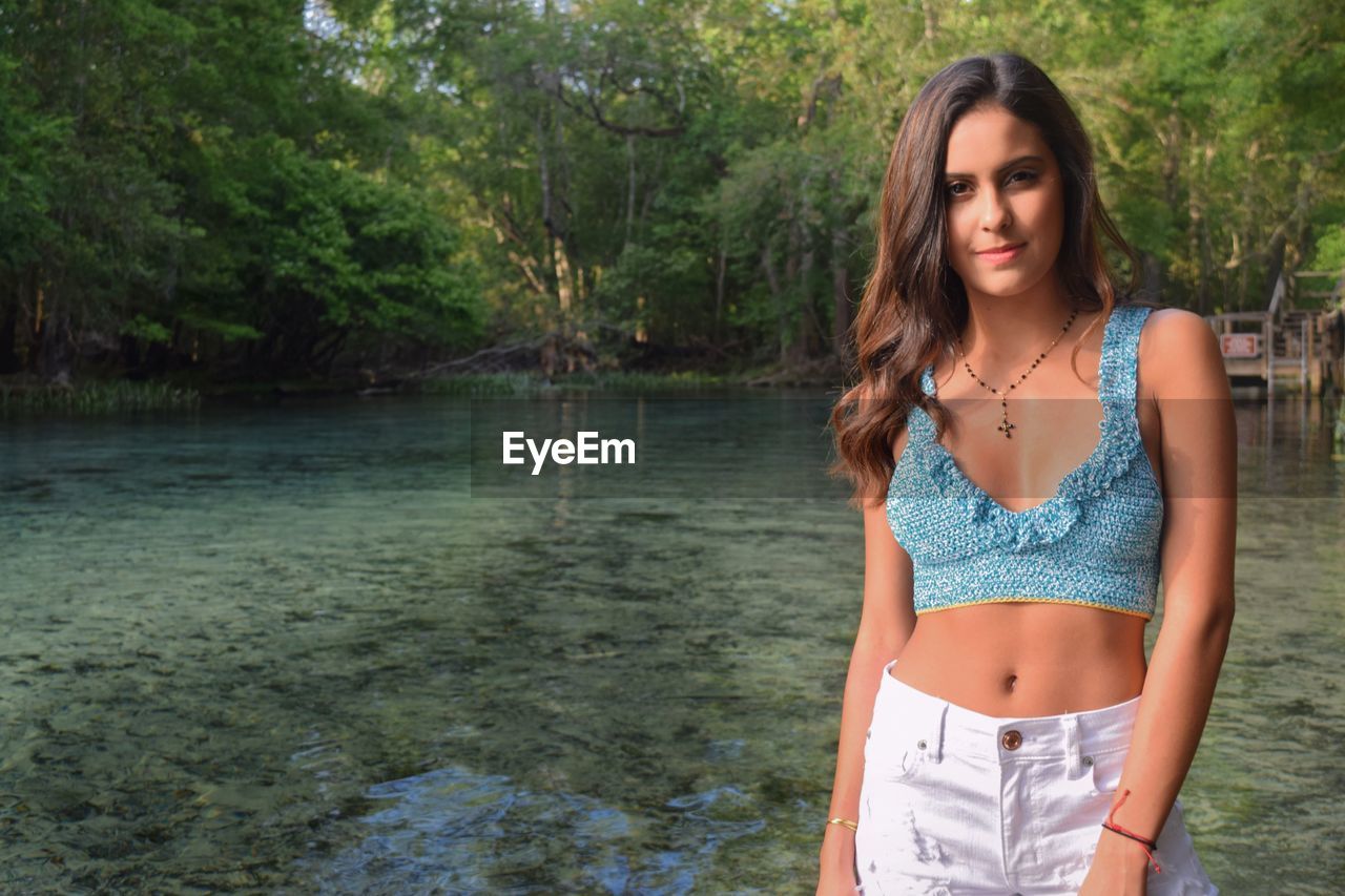 Portrait of beautiful young woman standing against lake